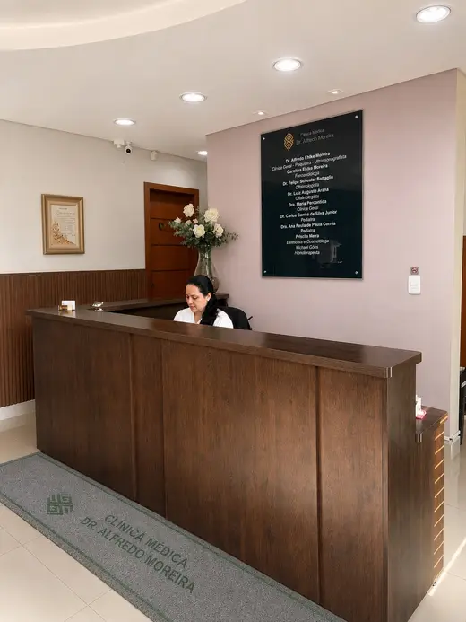 Recepção da clínica, com balcão de madeira e a placa do corpo clínico